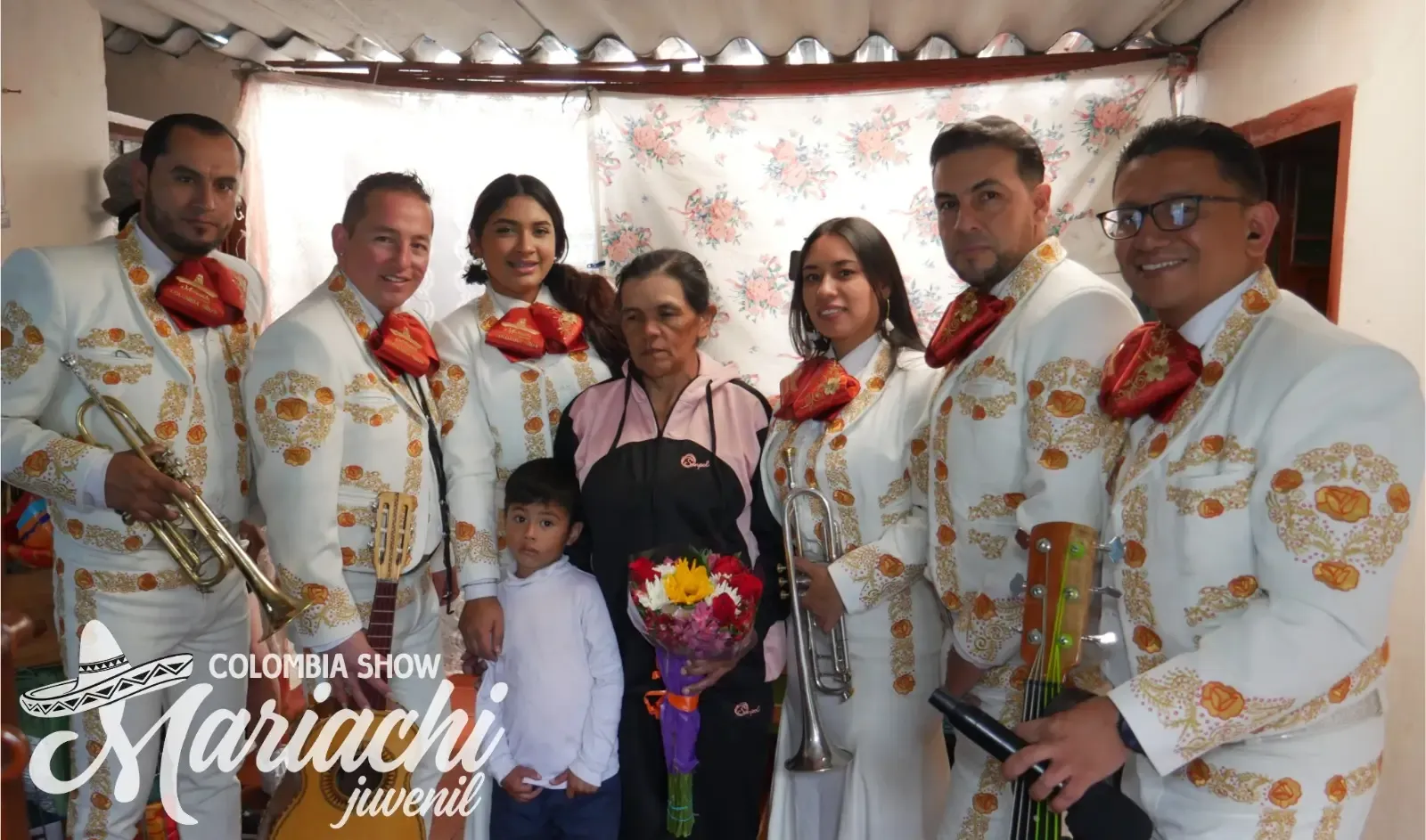 Grupo de mariachis completo posando con una familia y un ramo de flores en una casa de Bosa