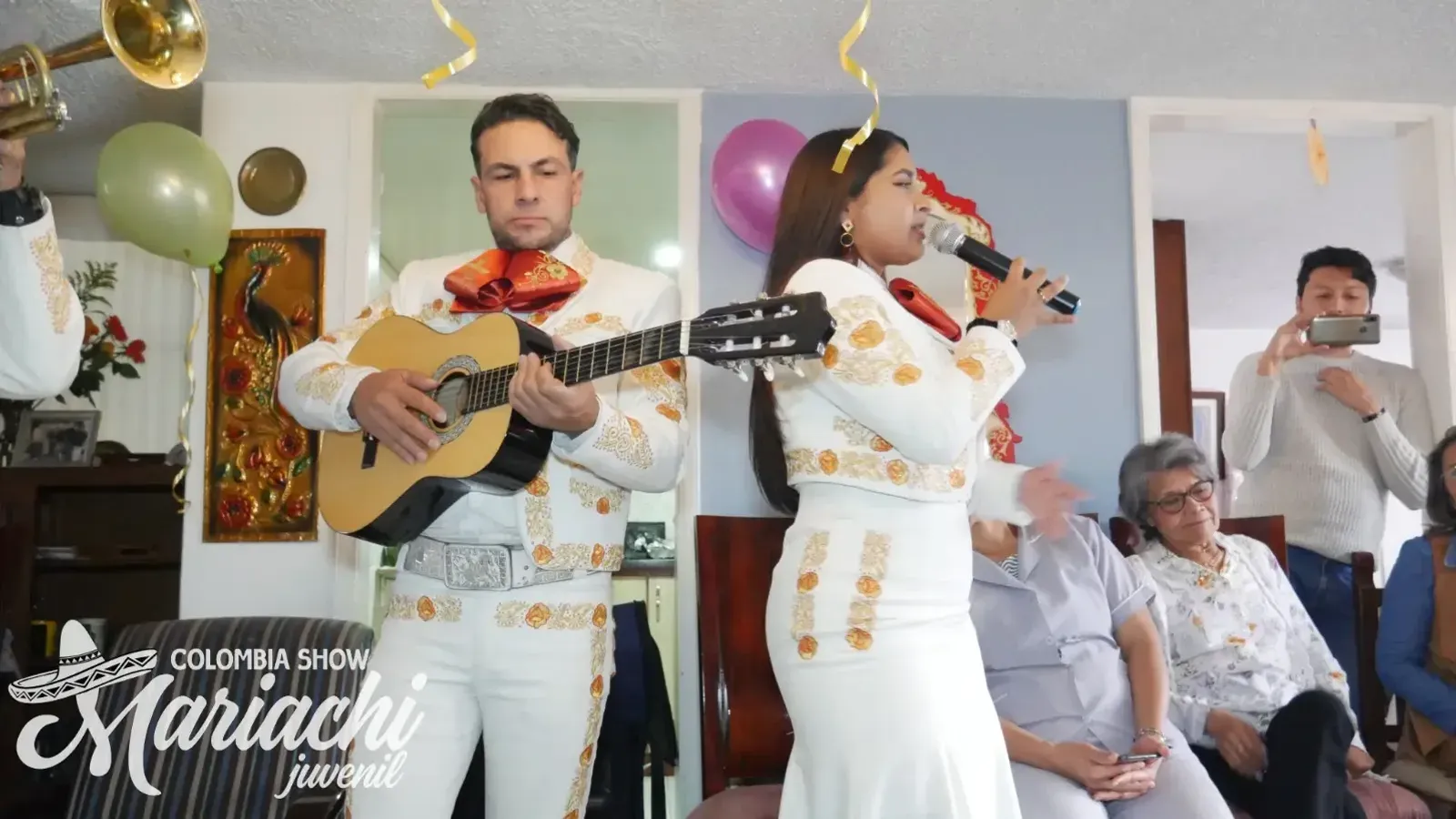 Mariachis cantando una serenata en la sala de una casa de Suba, con la familia sentada escuchando
