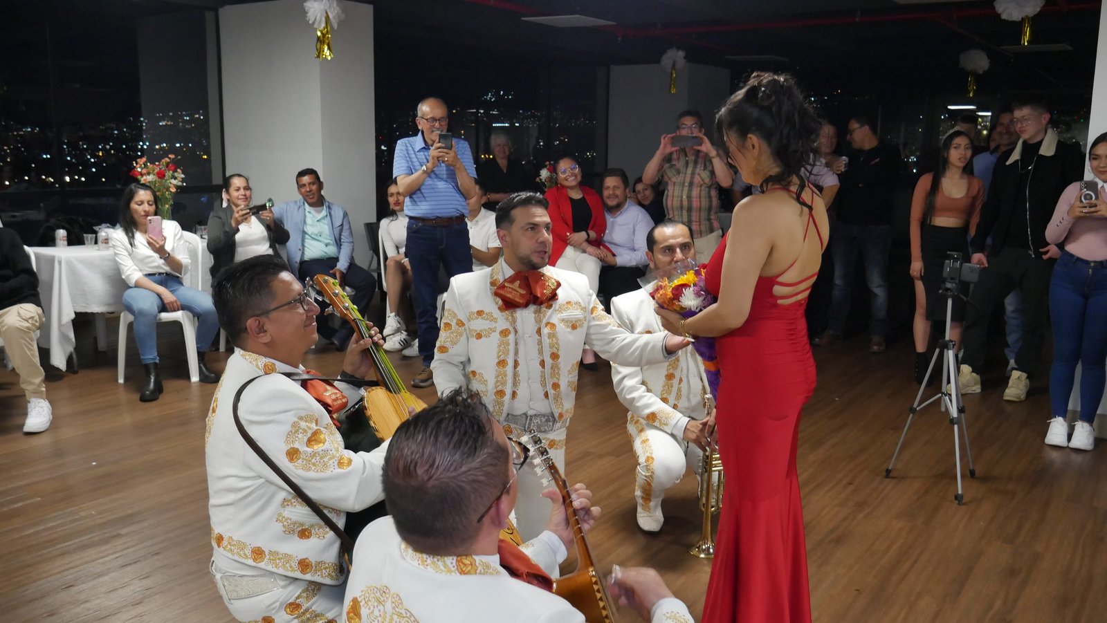 Músico de mariachi de rodillas entregando flores a Adriana en una serenata nocturna, Bogotá